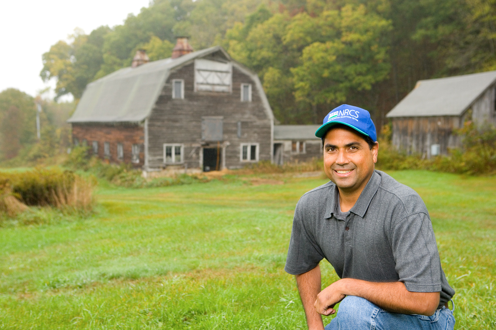 A man posing in front of a weathered barn